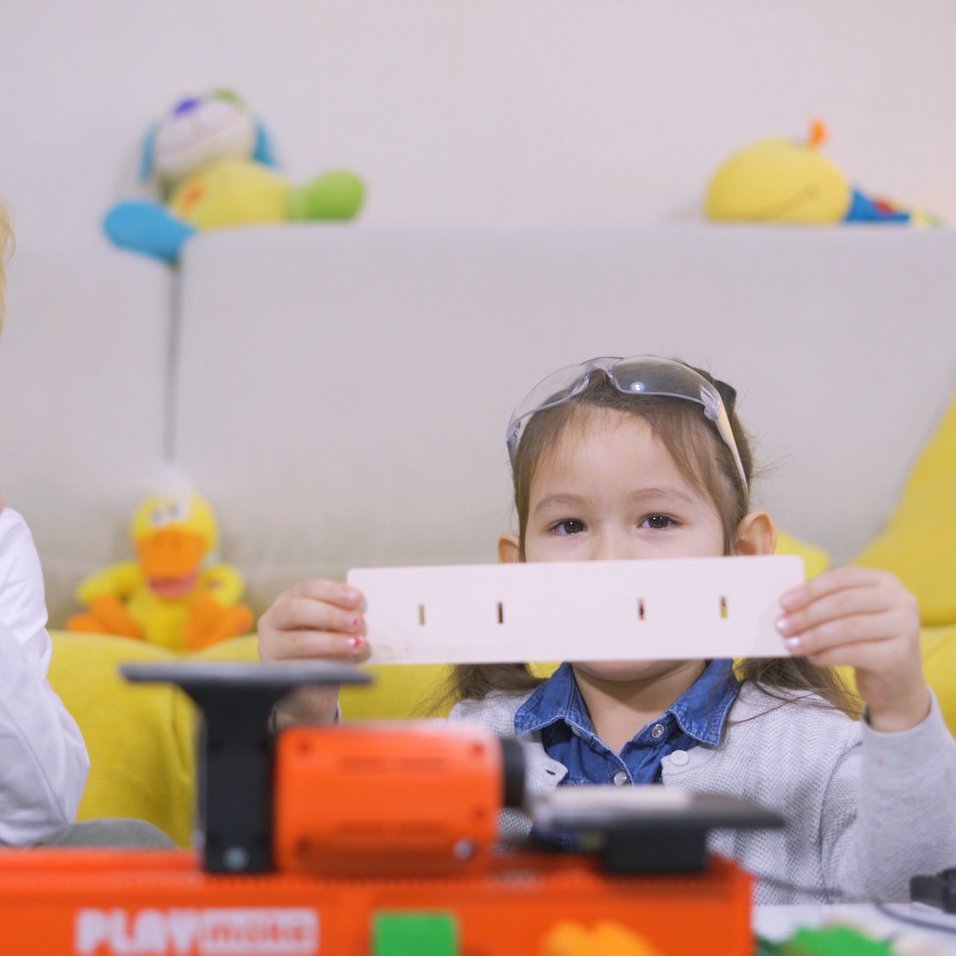 Kinder zeigen mit PLAYmake gemachte Modelle aus Holz mit der Maschine im Vordergrund